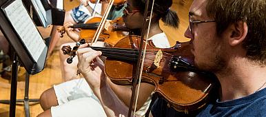 Image of students reading sheet music and playing violins.